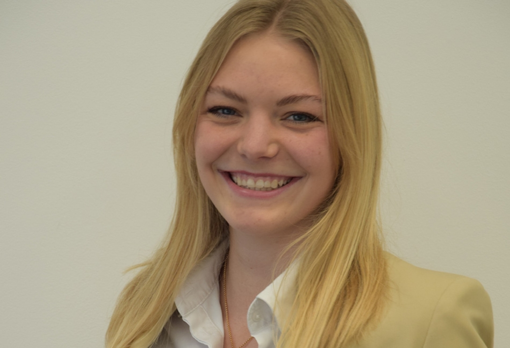 Joven rubia sonriendo a la cámara, con una chaqueta y camisa blanca.