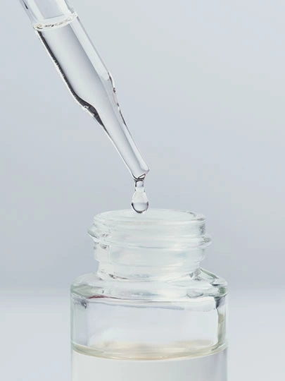 Gota cayendo de una pipeta en una botella de vidrio con líquido.
