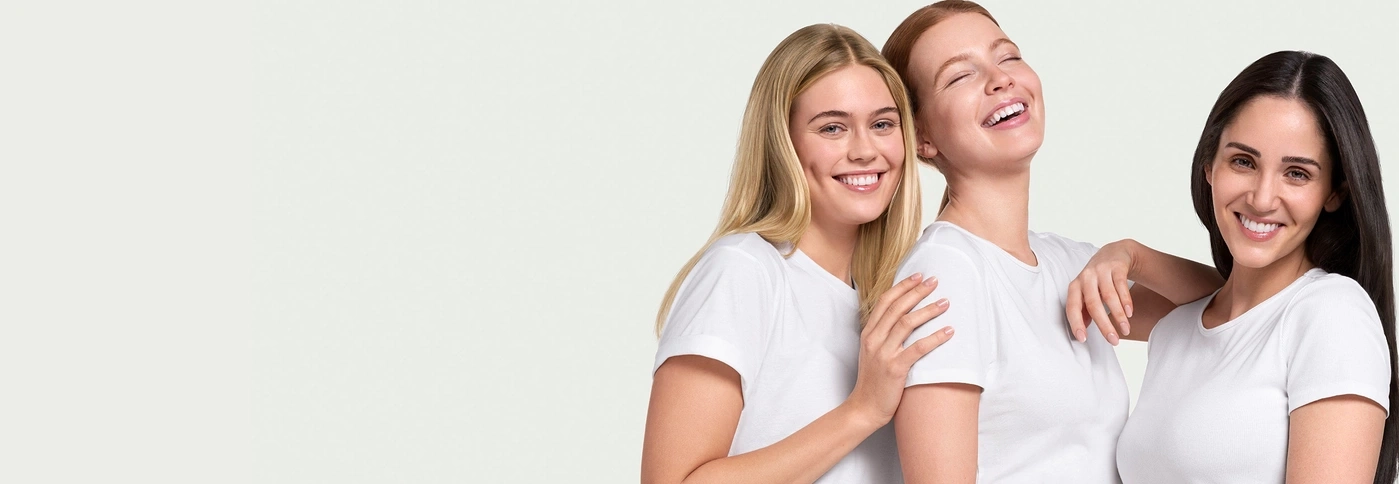 Three smiling women in white t-shirts, embracing and having fun together.