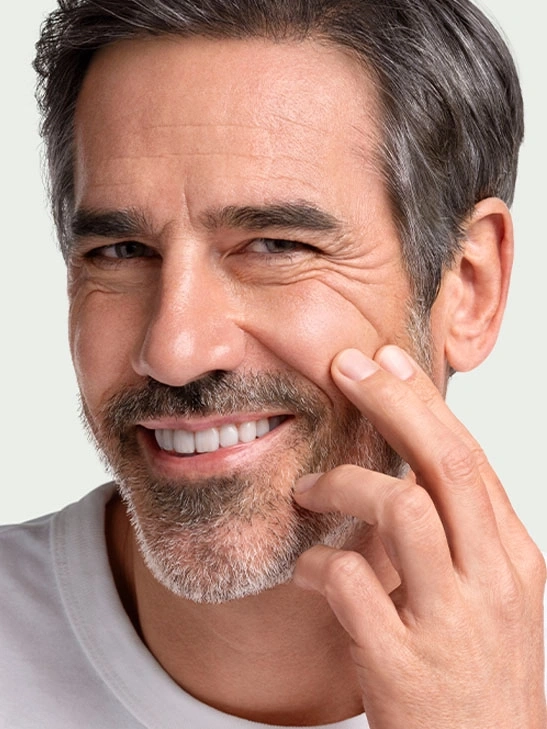 Smiling man with wrinkles touching skin and a beard, looking at the camera.