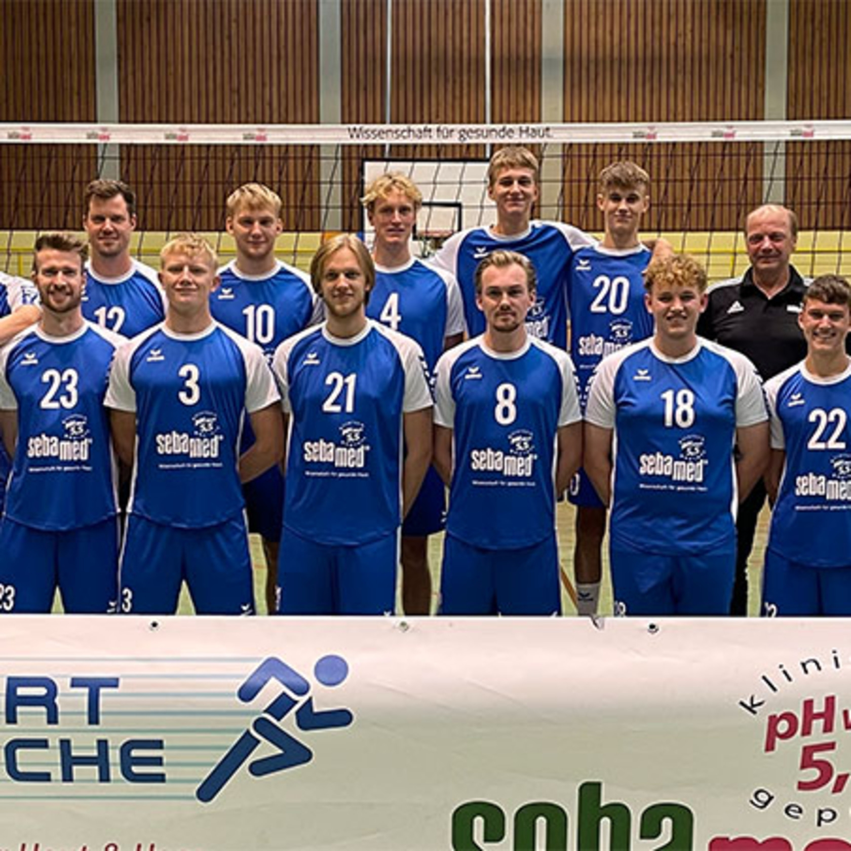 Volleyball team in blue jerseys with advertisement, posing for a photo.