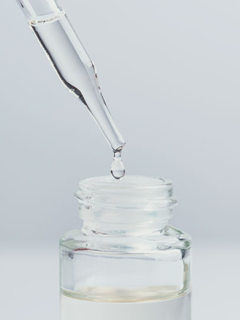Droplet falling from a pipette into a glass bottle with liquid inside.