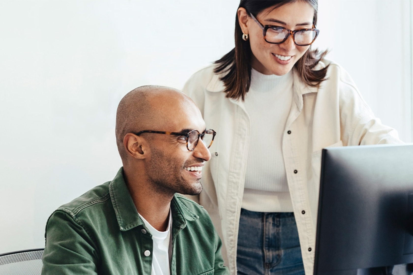 Dos personas trabajando juntas en una computadora, sonriendo.