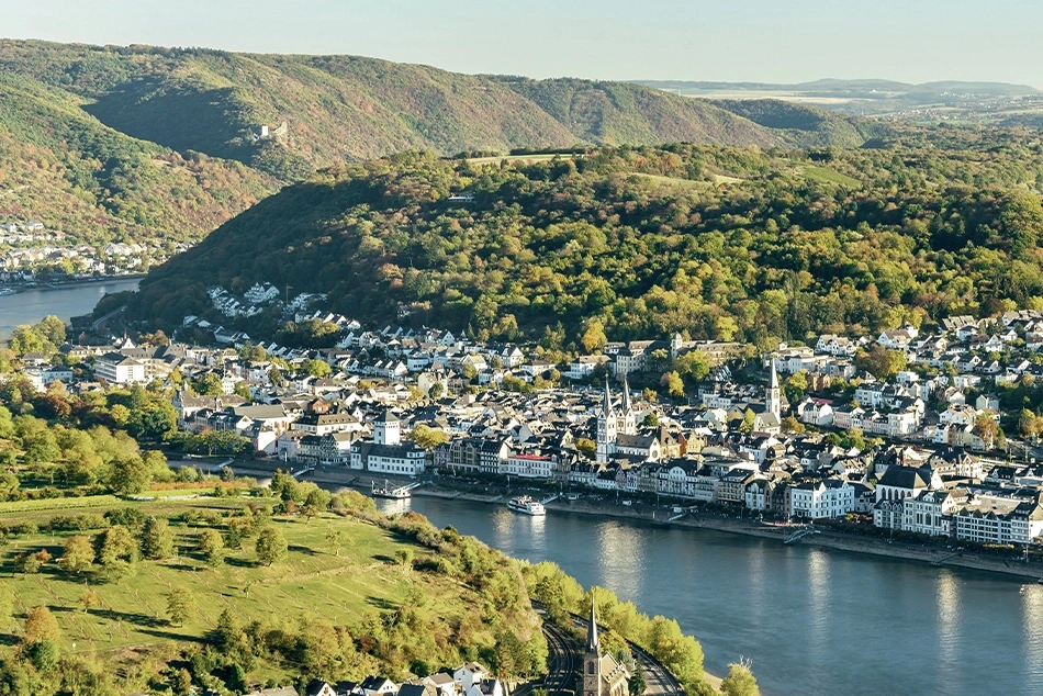 Luftaufnahme einer malerischen Stadt am Flussufer, umgeben von grünen Hügeln und Bäumen.