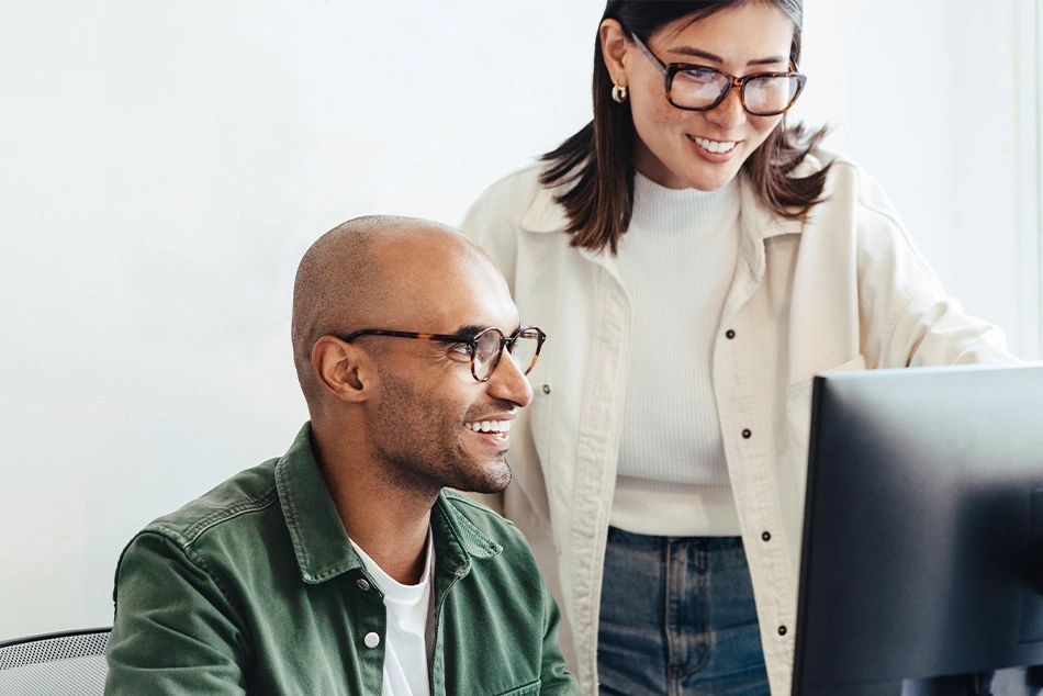 Dos personas trabajando juntas en una computadora, sonriendo.