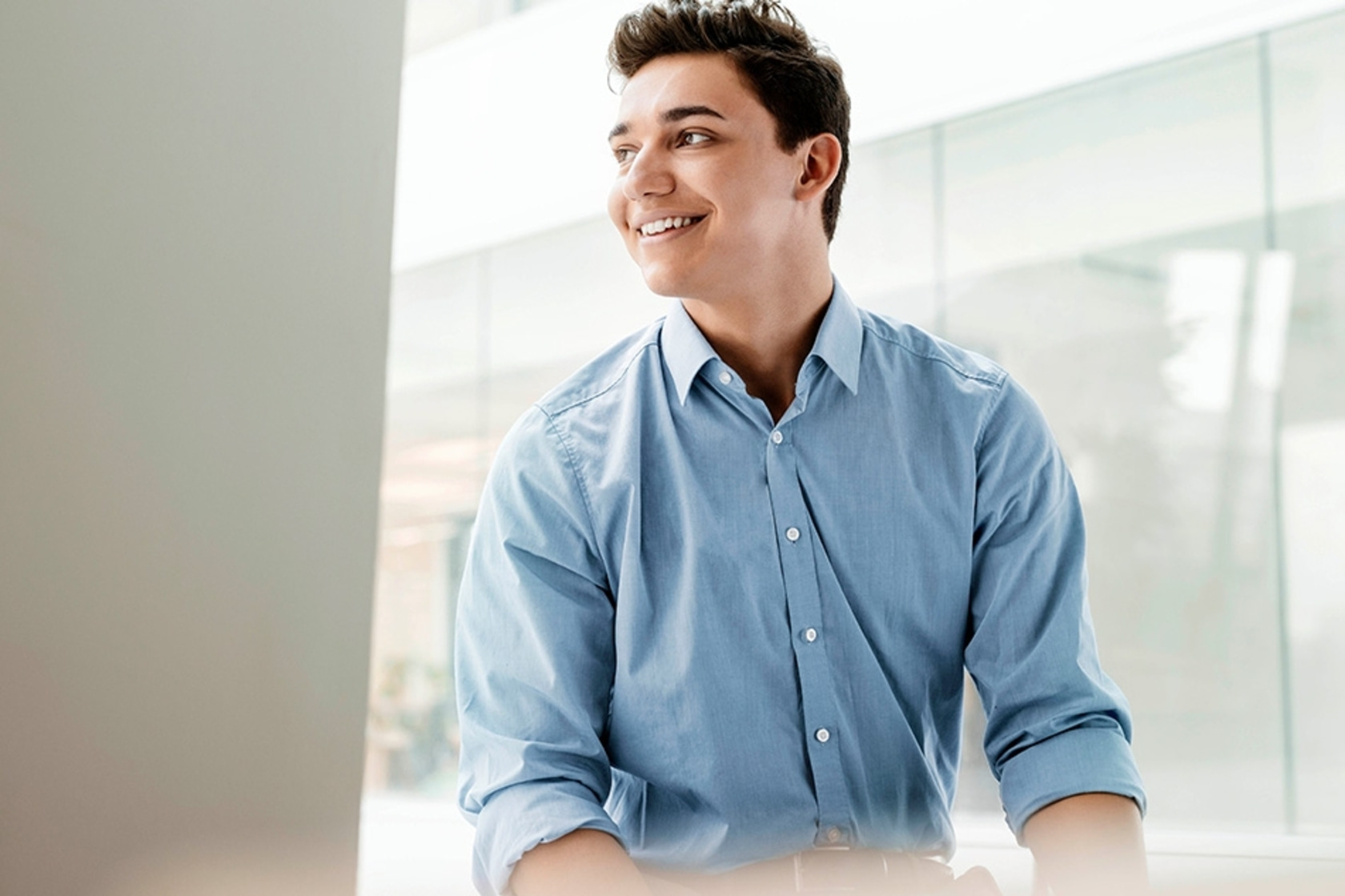 Un hombre sonriente con camisa azul mirando por la ventana.