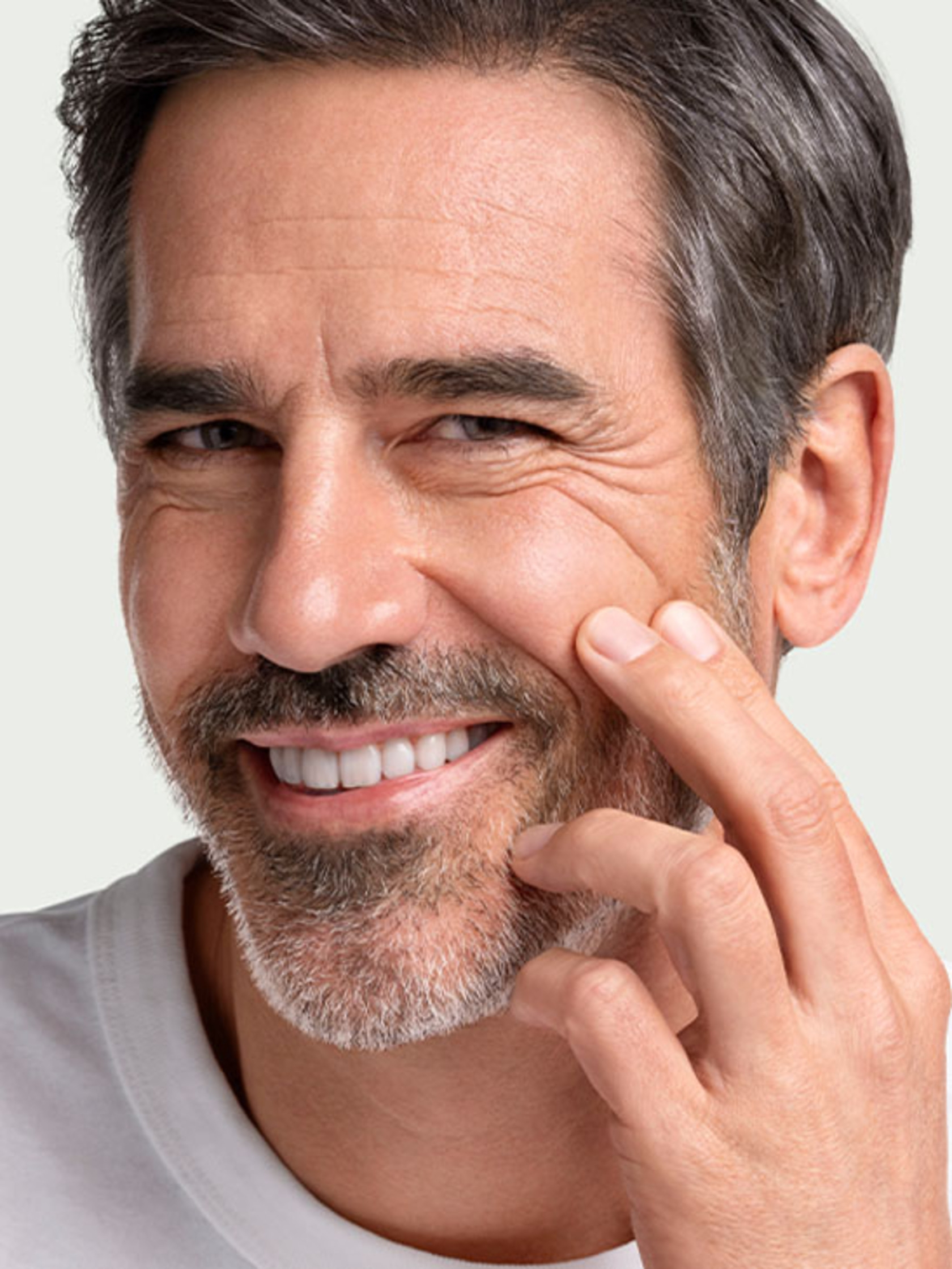 Smiling man with wrinkles touching skin and a beard, looking at the camera.