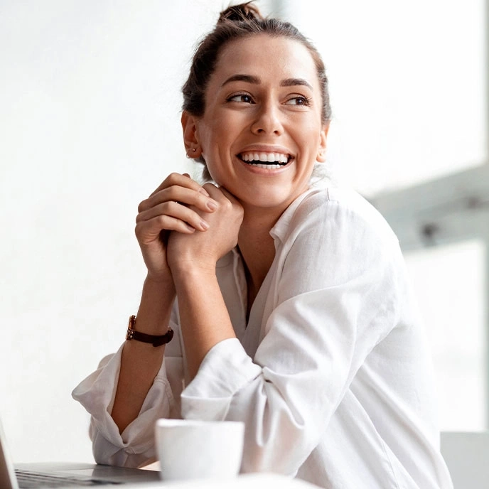 Smiling woman with hands under chin looking thoughtful and happy.