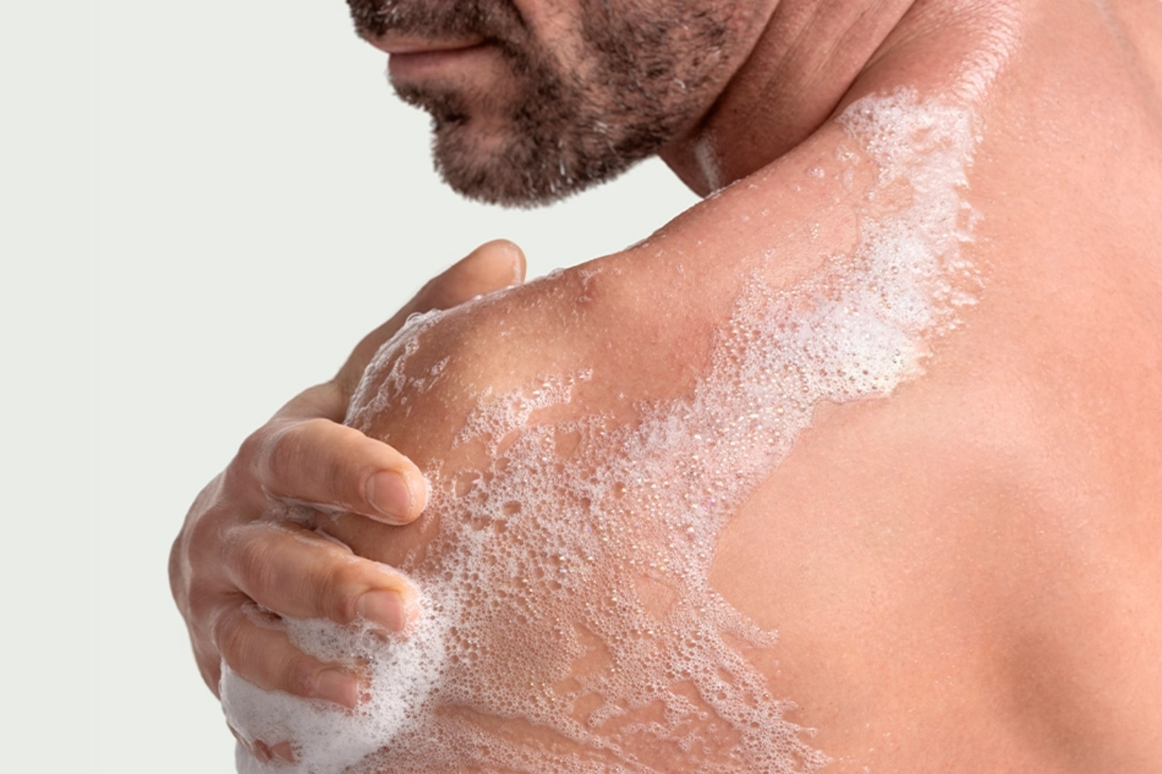 Man washing with soap in shower, foam on skin, close up of body