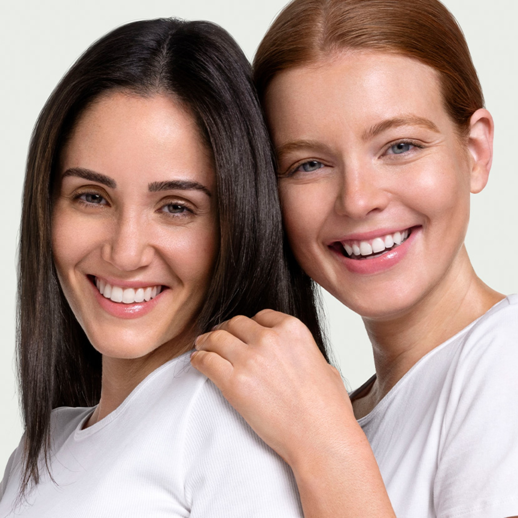 Two smiling women in white t-shirts, embracing and smiling happily together.