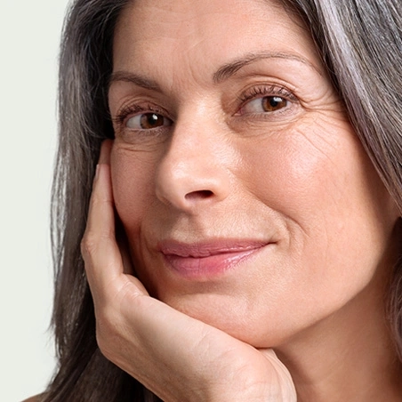Portrait of an older woman with her hand on her chin, smiling and looking